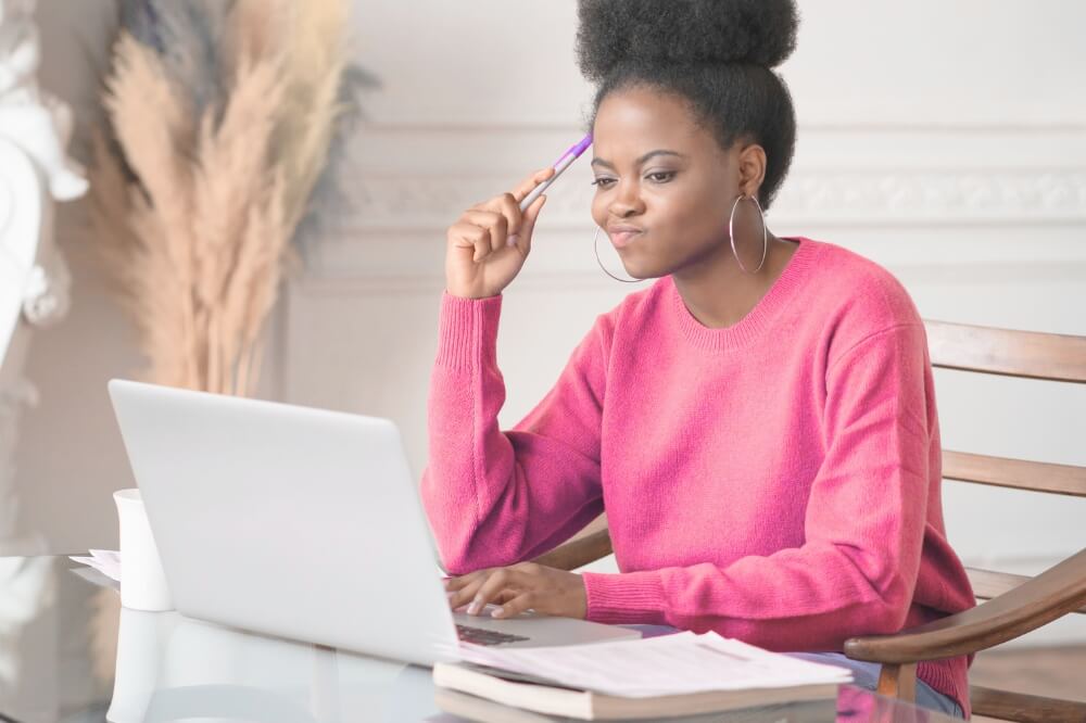 a woman is thinking while working on her laptop